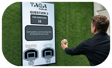 A guest throwing a softball at a large digital Truth or Myth display screen to lock in an answer at a high-energy corporate exhibition booth activation